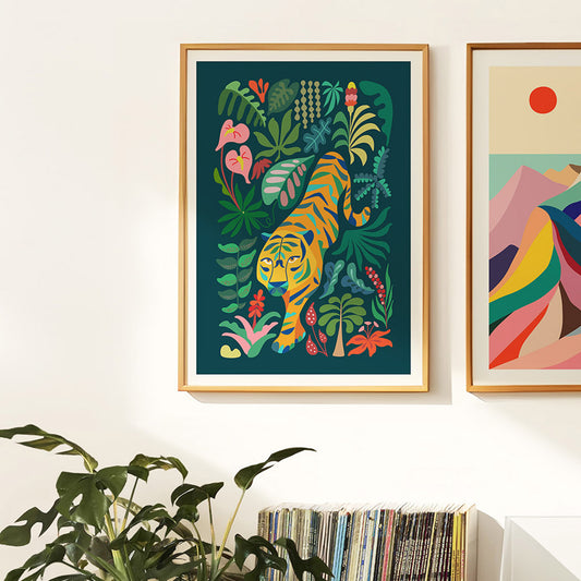 Two framed art prints on a wall with plants and a book. One of the prints is a tropical tiger design.