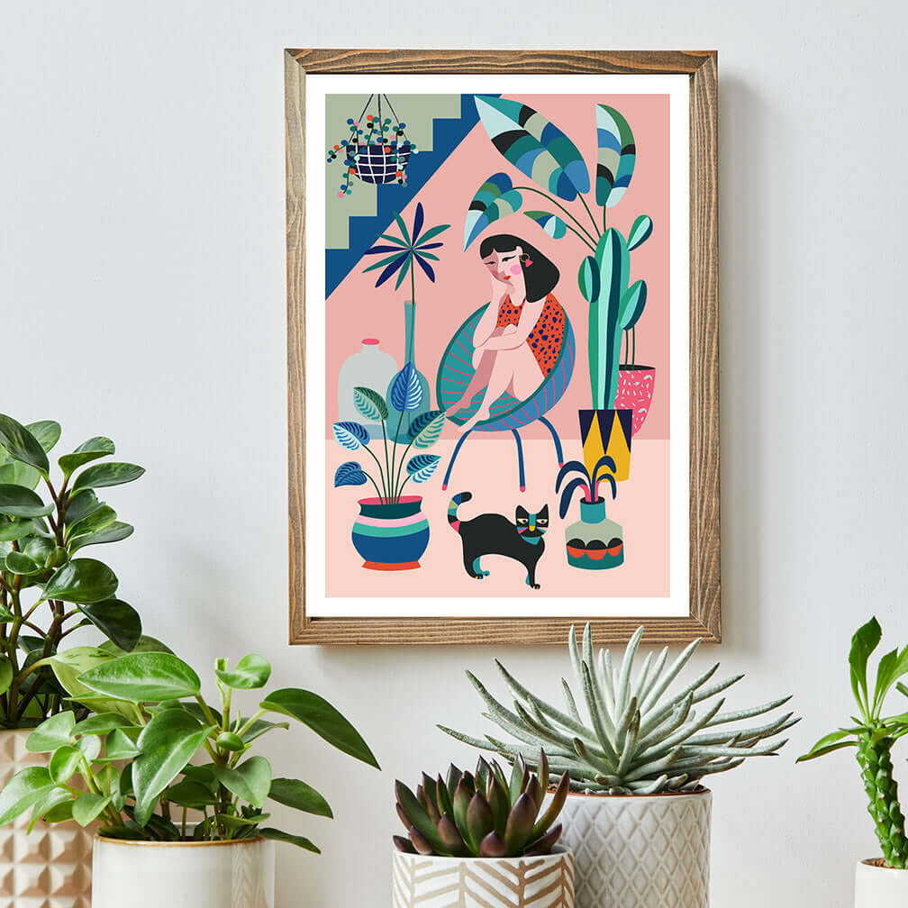 The Print featuring a Woman is sitting on a chair and a cat standing on the floor. this print on a table surrounded by plants.