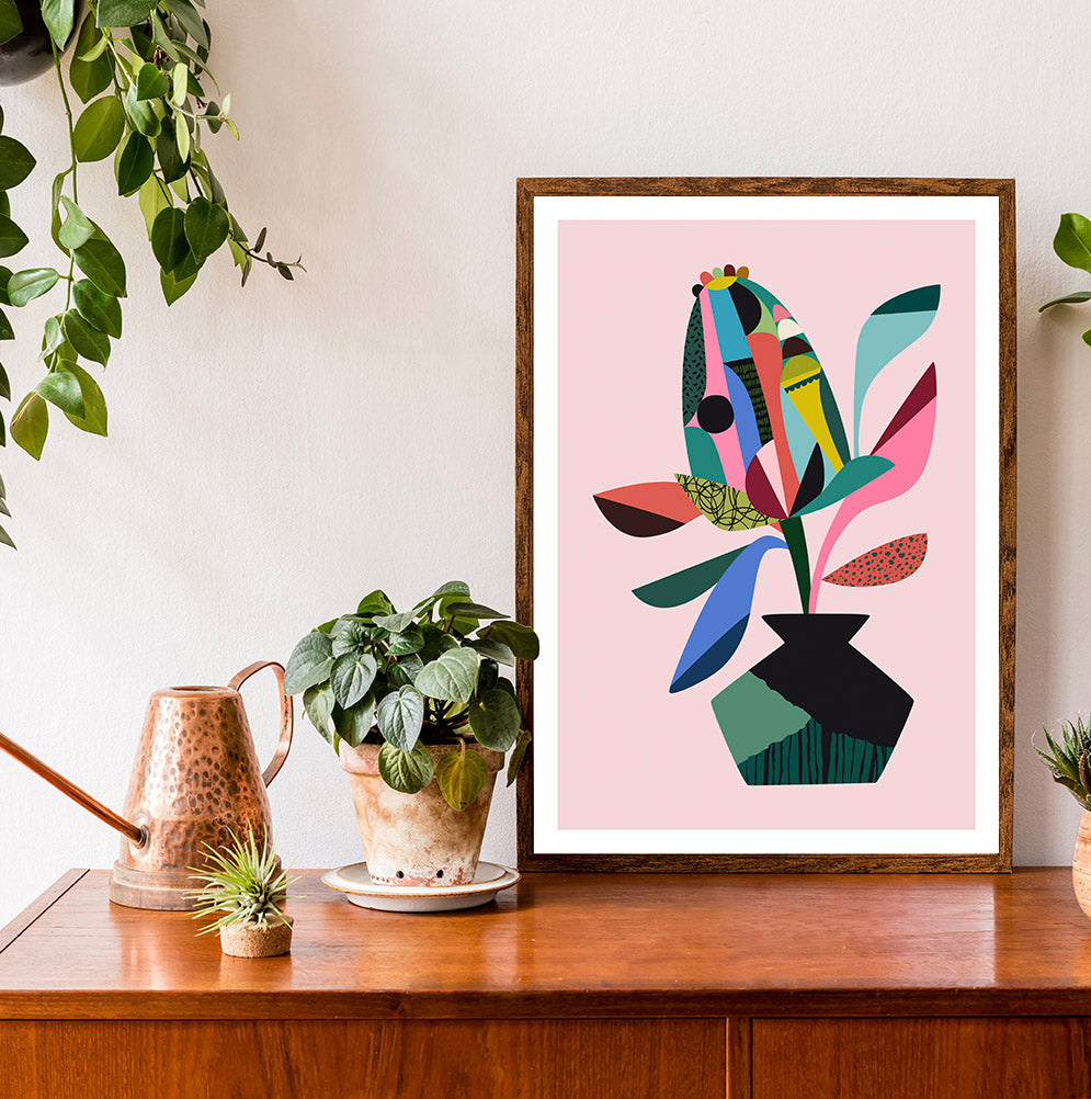 A vibrant abstract Banksia art print in pink and blue, placed on a wooden table.