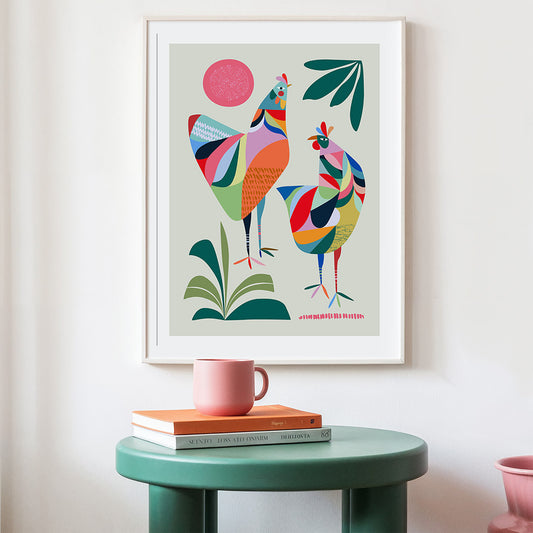 Colorful abstract art print of two birds on a wall above a green table with books and a mug.