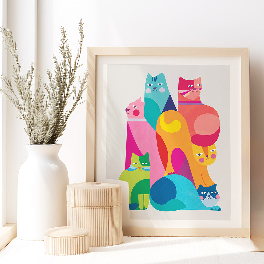 Framed colorful cat illustration on a white wall with decorative items.
