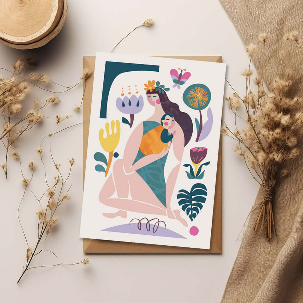 A greeting card featuring a woman is holding a baby and surrounded by vibrant flowers.