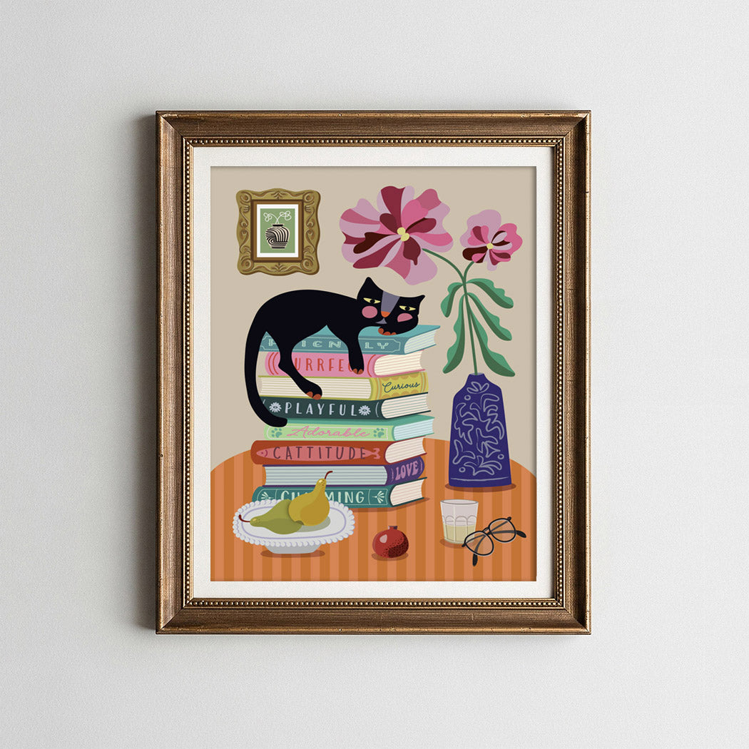 Framed artwork of a black cat on books with flowers and a vase.